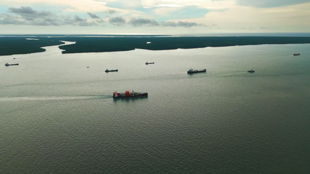 Aerial: cargo ships on the Strait of Malacca at sunset next to the Royal City of Klang Port in the state of Selangor, Malaysia, establishing drone shot
