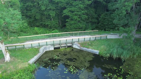 "Drone-glides-over-Europe's-dawn-lit-lake,-capturing-a-tranquil-lagoon,-lush-forest,-and-an-elegant-bridge