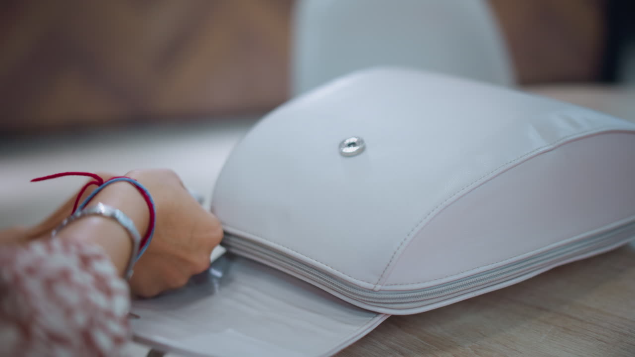 손이 테이블 위에 세련된  가방을 열고 손과 가방 세부 사항에 초점을 맞추고, 손목밴드와 팔를 보여주는 손의 클로즈업