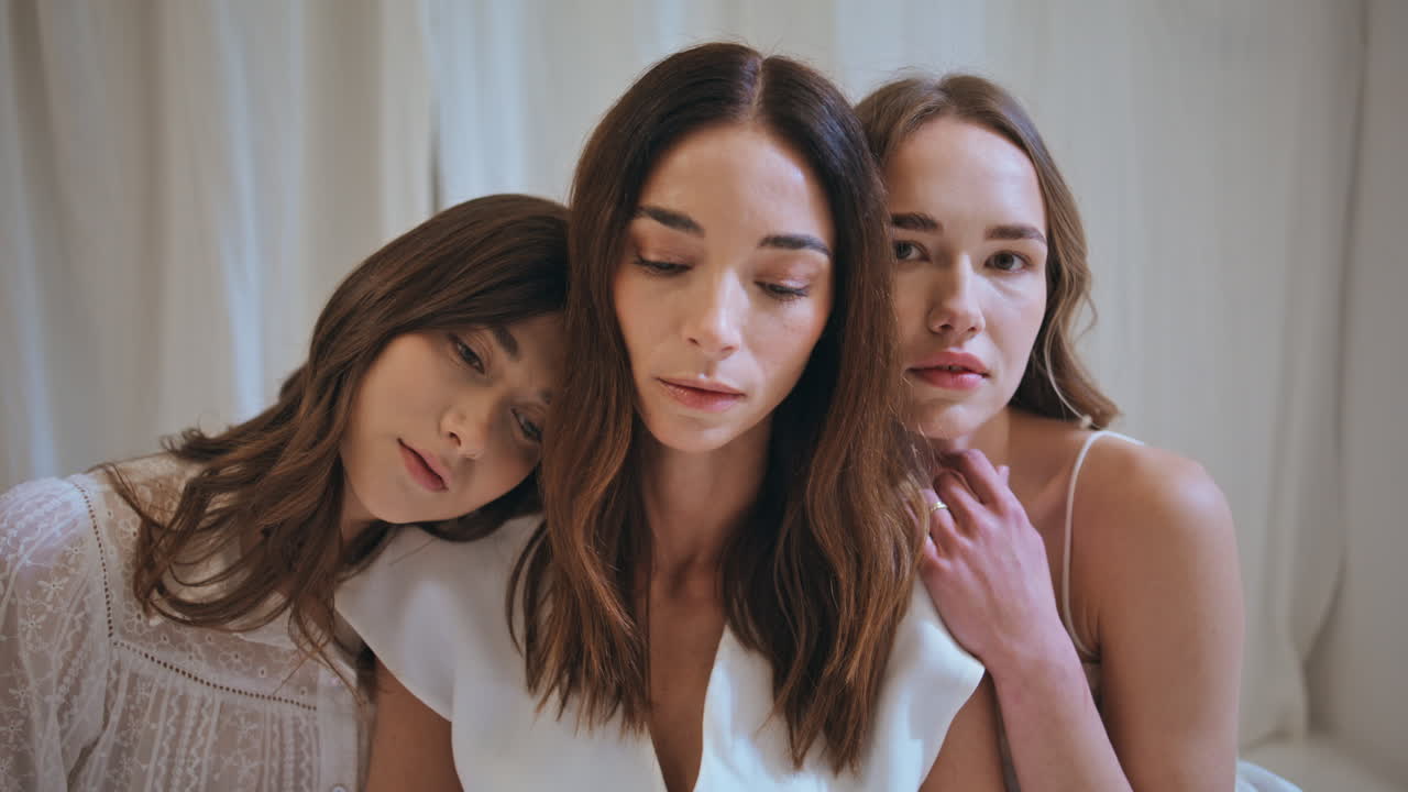 쾌적한 방에서 포옹하는 세 명의 여성의 초상화. 평온하고 아름다운 소녀들이 카메라를 바라보고 있습니다.
