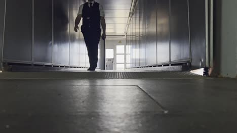 low-angle shot of a male airport worker in uniform walking towards the camera inside a metallic loading bridge tunnel. for travel, airport operations, and transport concepts