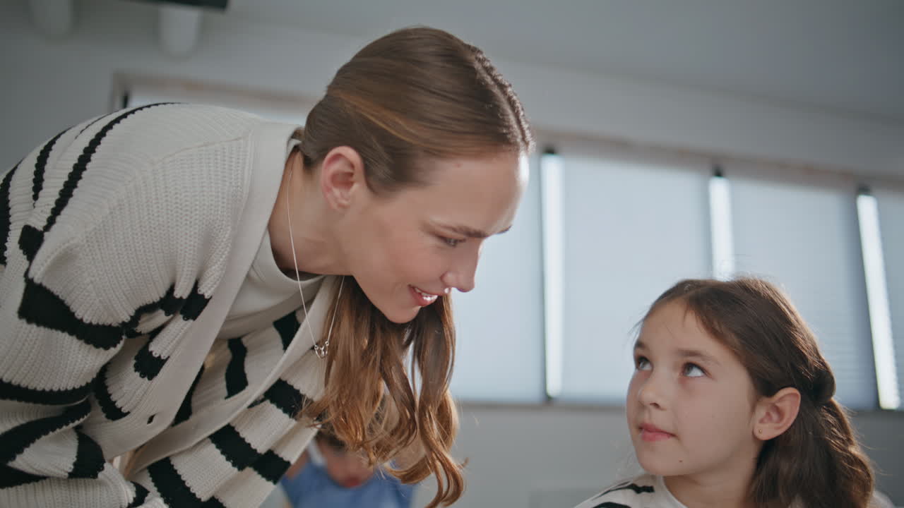 Smiling teacher talking child girl at table in classroom closeup. Pupil lesson