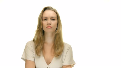 A-close-up-of-a-woman-with-an-annoyed-facial-expression,-raising-her-finger-to-her-mouth-and-making-a-shushing-expression,-on-a-seamless-white-studio-background