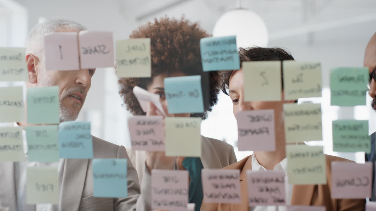corporate business team using sticky notes brainstorming problem solving strategy on glass whiteboard working on deadline in office meeting