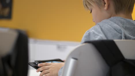 Rear-view-of-caucasian-school-boy-studying-on-tablet-in-classroom,-Static