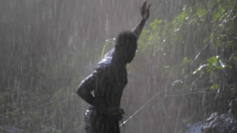 close up cámara lenta de un hombre africano feliz bailando bajo el spray de una cascada tropical mientras se moja