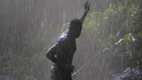 close up slow motion shot of a happy african man dancing under the spray of a tropical waterfall while getting wet