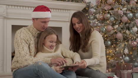 father, mother and daughter playing with a tablet at christmas wearing a santa's hat