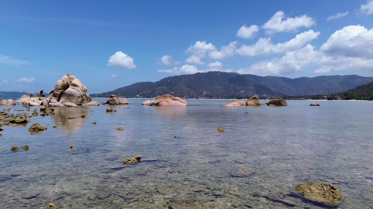 Aerial drone footage of Lamai Beach, Koh Samui, Thailand, showcasing rocky coastline, turquoise ocean water, lush green mountains, and scenic tropical island horizon under a clear sky