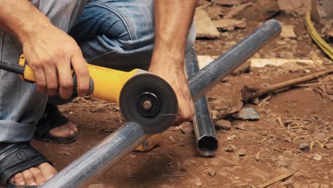 Hombre-Cortando-Un-Tubo-De-Acero-Galvanizado-Con-Una-Amoladora-Angular-Eléctrica-Industrial-Para-Elaborar-Una-Estructura-Metálica-En-Un-Lugar-De-Construcción-En-Un-Entorno-Rural