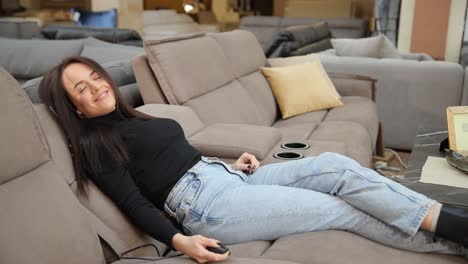 a woman tests couches comfort in a store by sitting laying down with a remote a woman is testing couches in a furniture store sitting and laying down with a remote control she seems to shop for furniture and check the comfort of each couch