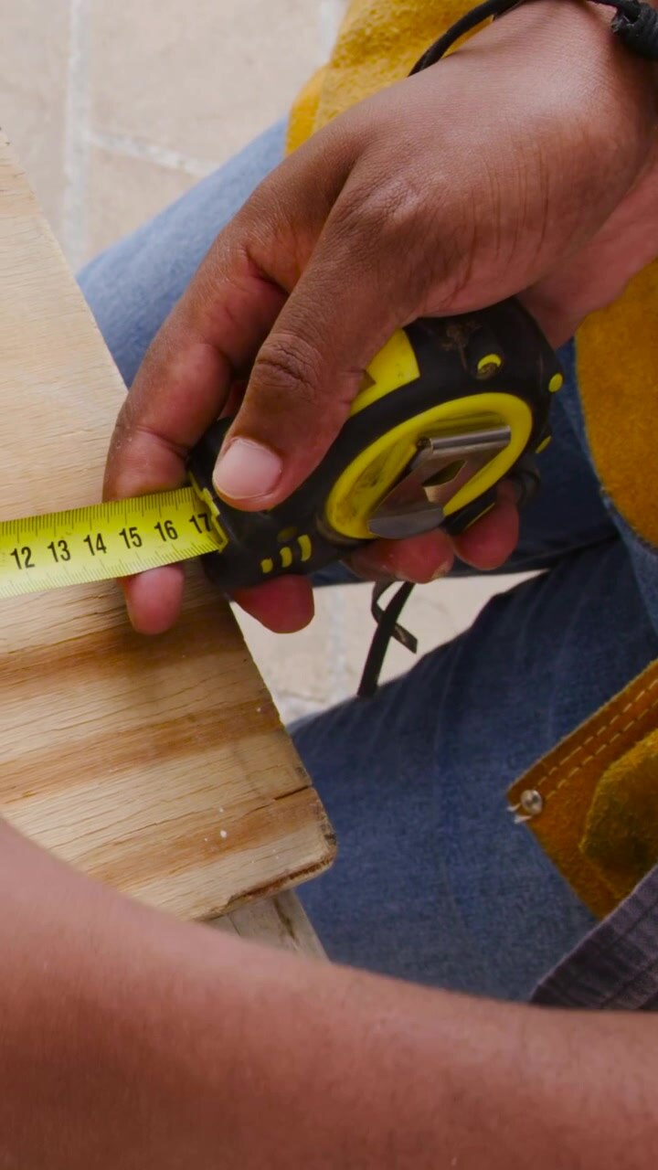 Vertical video: Reaching into yellow tool belt, worker pulling tape measure, marking plank on porch