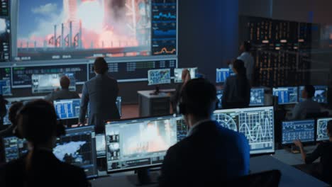 group of people in mission control center witness successful space rocket launch. flight control employees sit in front computer displays and monitor the crewed mission. team stand up and clap hands.