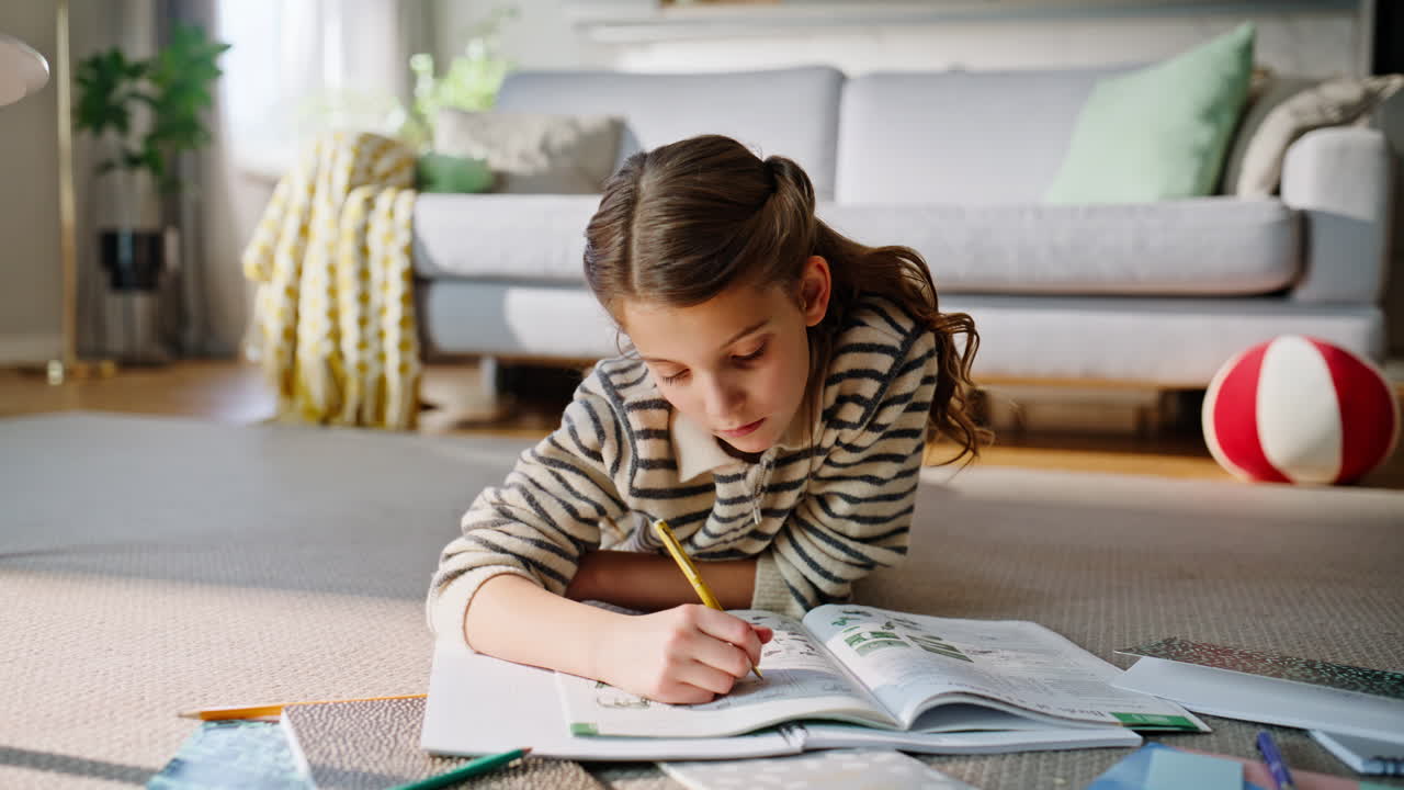 Pensive girl completing homework lying carpet closeup. Child writing notebook