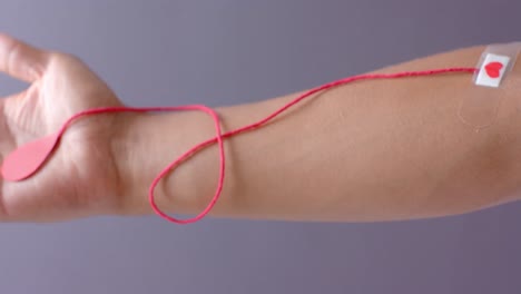 hand of biracial man with blood drop, red string and heart sticking plaster on grey, slow motion