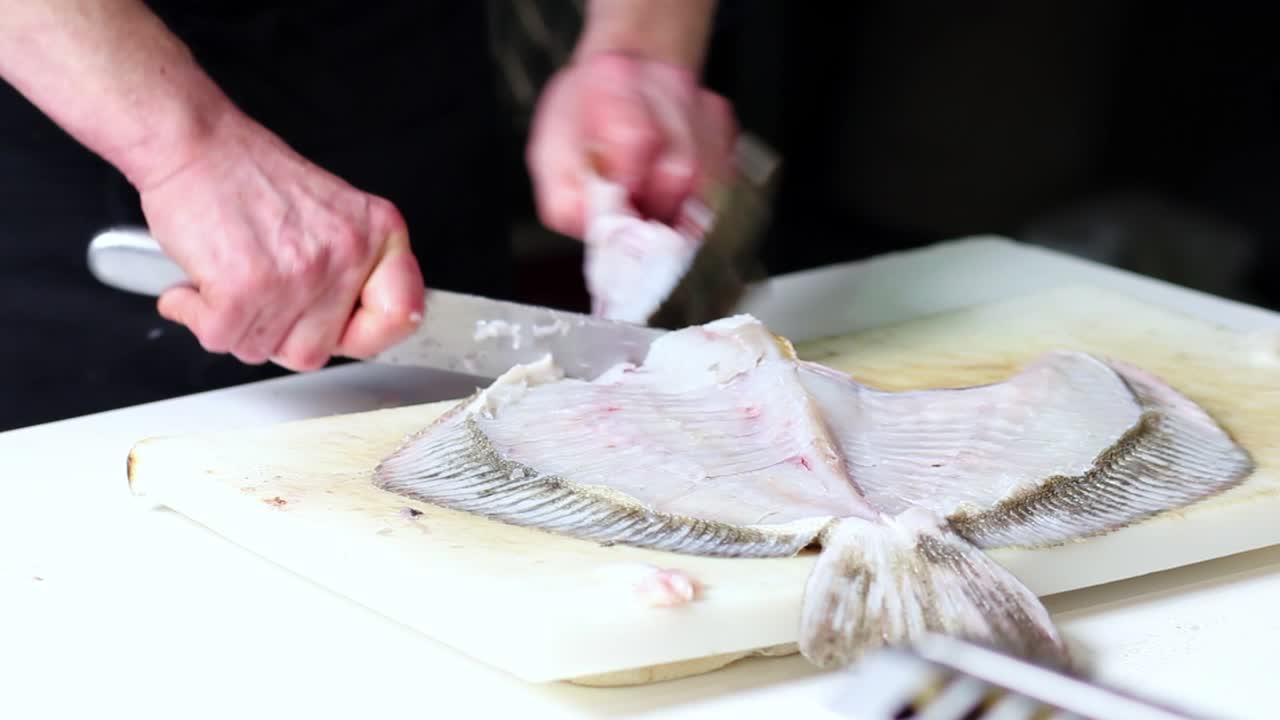 un vendedor de pescado limpia un buen rape con un cuchillo de cocina, sobre una tabla de cortar blanca