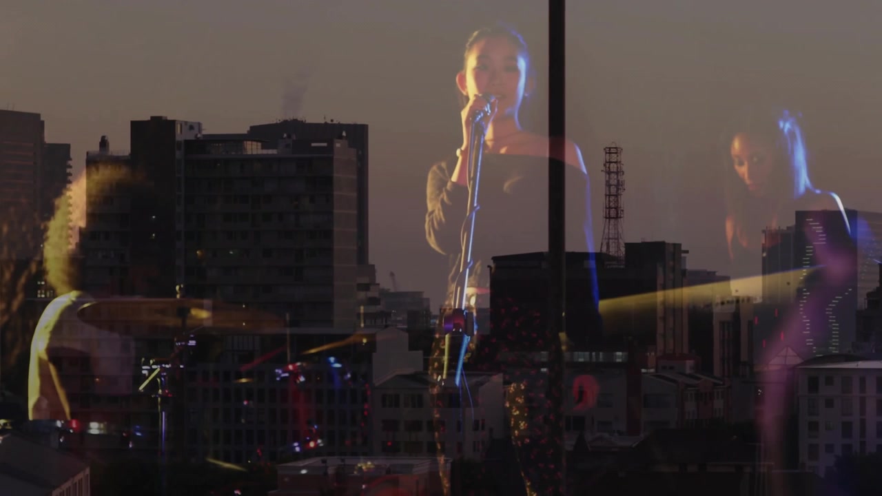 Bandmates performing over skyline with instruments appearing, tapping drums, singing, playing keys
