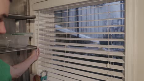 a guy rotating the twist wand to open the slats of the window blinds in the kitchen - close up shot