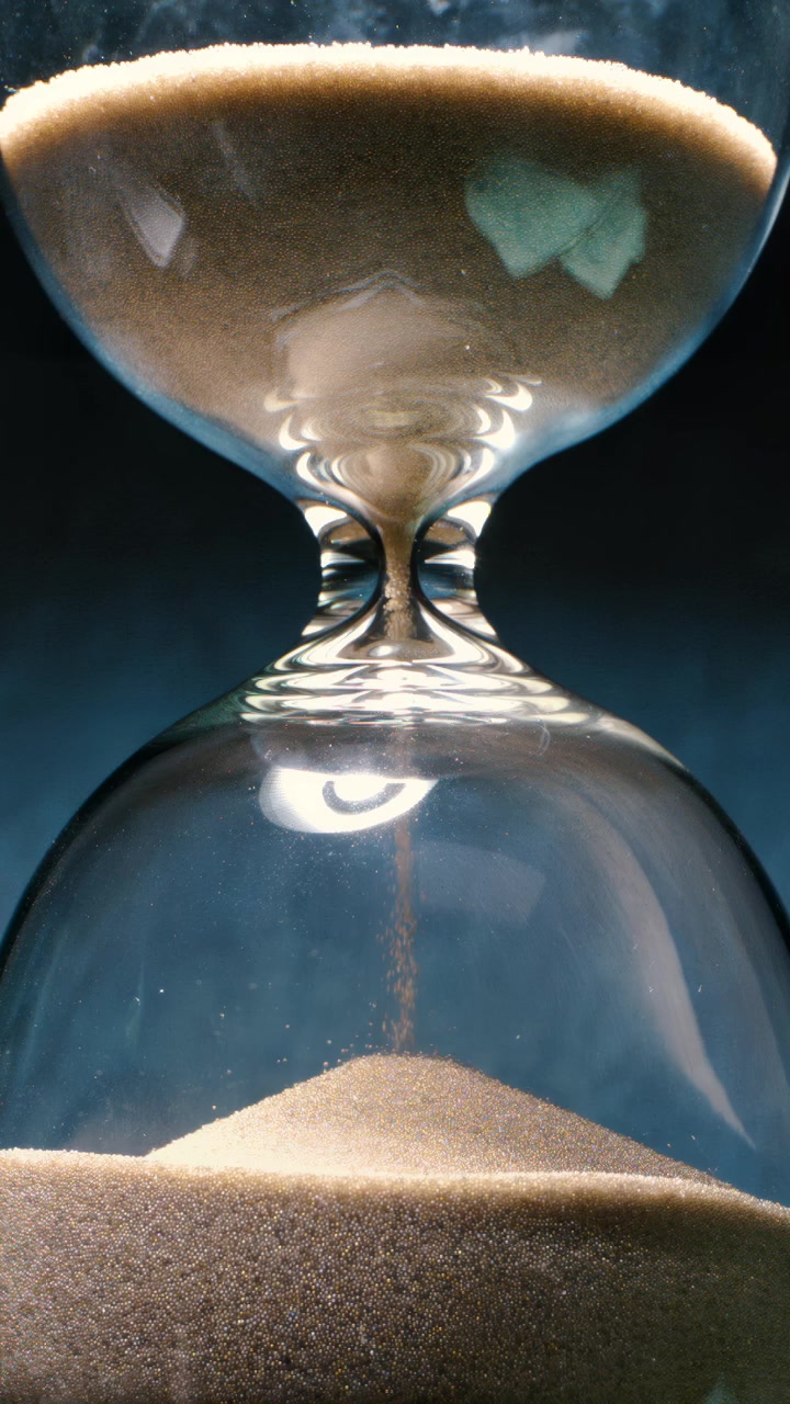 Concept of turning back time. Hourglass with grains of sand on a dark background. Shot on super slow motion camera 1000 fps.