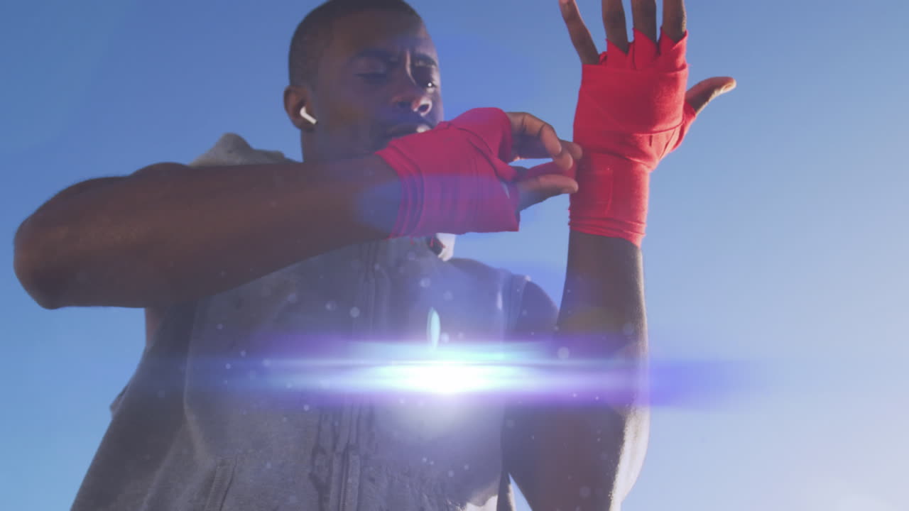 Animation of glowing lights over african american man training in sun wrapping hands