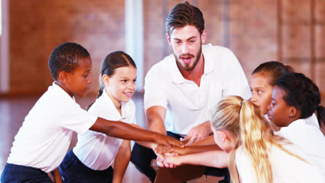 Sports-teacher-and-school-kids-stacking-hands-in-basketball-court