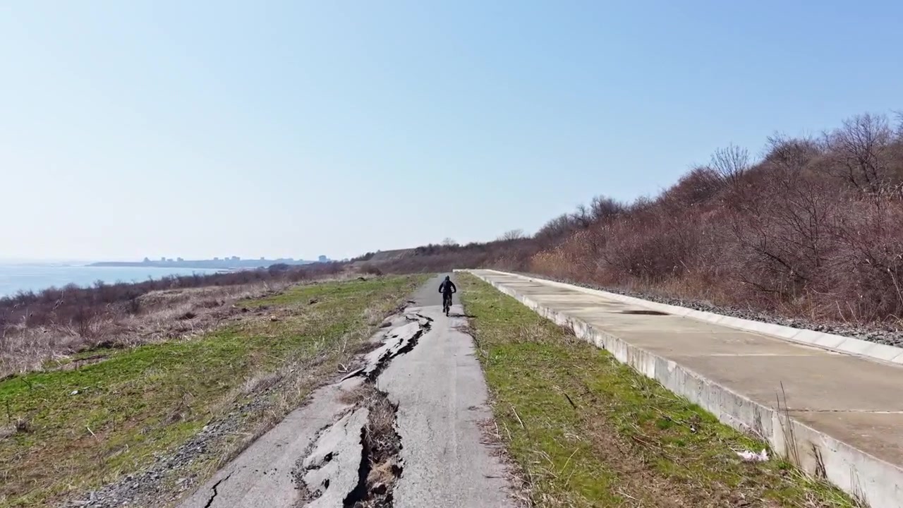 Dlouhá popraskaná cesta vede k vodě s osamělou osobou kráčející za jasného denního světla na okraji přírodní oblasti.