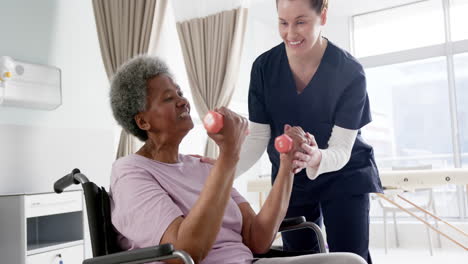 Mujer-Mayor-Diversa-Haciendo-Ejercicio-Con-Pesas-Y-Doctora-Asesorando-En-El-Hospital,-Cámara-Lenta