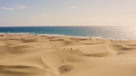 Drone-shot-of-dunes-and-desert-with-beach-in-the-background,-dunas-de-maspalomas,-gran-canaria