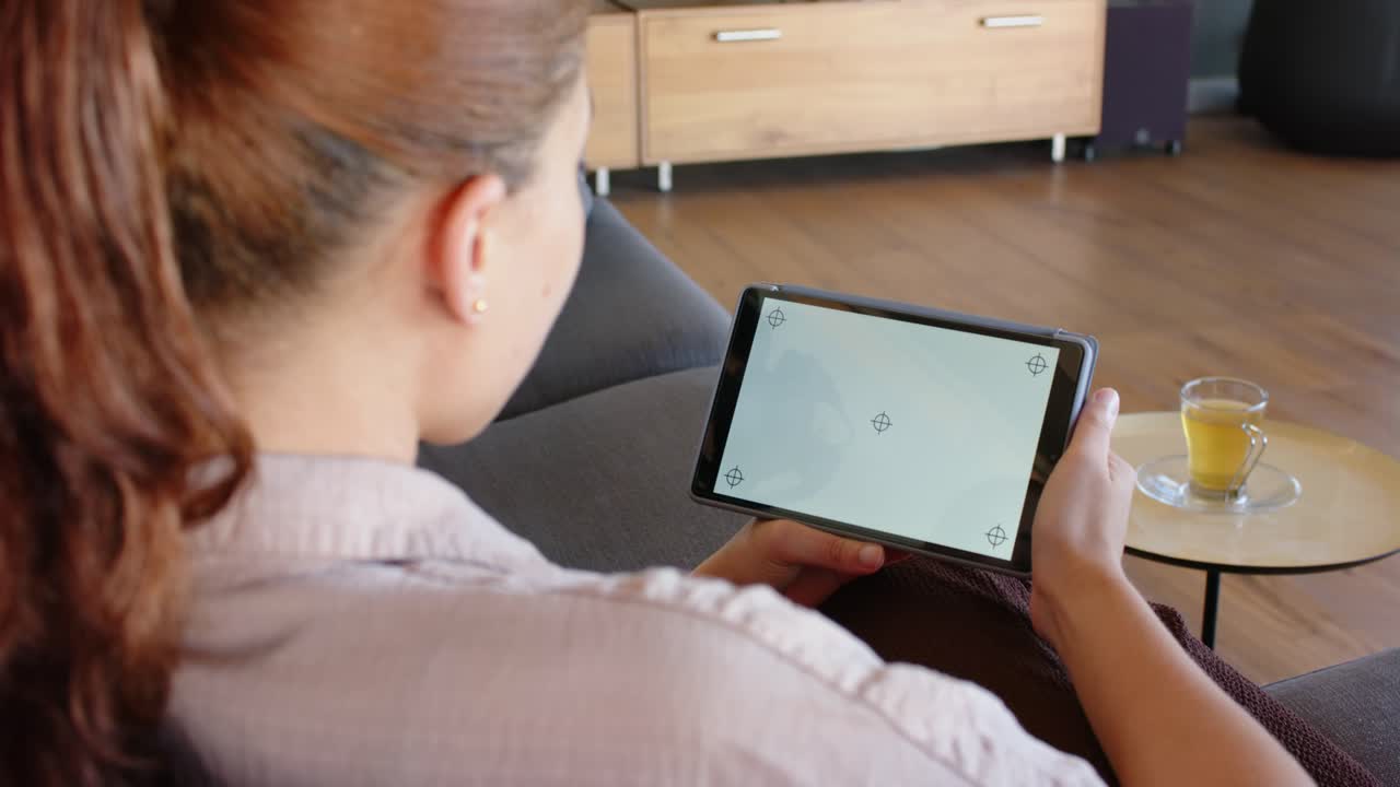 African American woman seeing markers, adjusting tablet angle to align screen on sofa in pale top