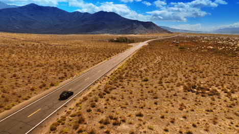 catching up with a black car driving by the empty highway in the desert. some huts are at the wayside. top view.