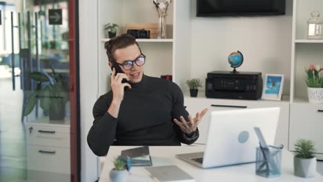 el hombre está sentado en su escritorio de trabajo, contestando el teléfono, sonriendo ocasionalmente, buscando en su tableta y pareciendo estresado y ocupado