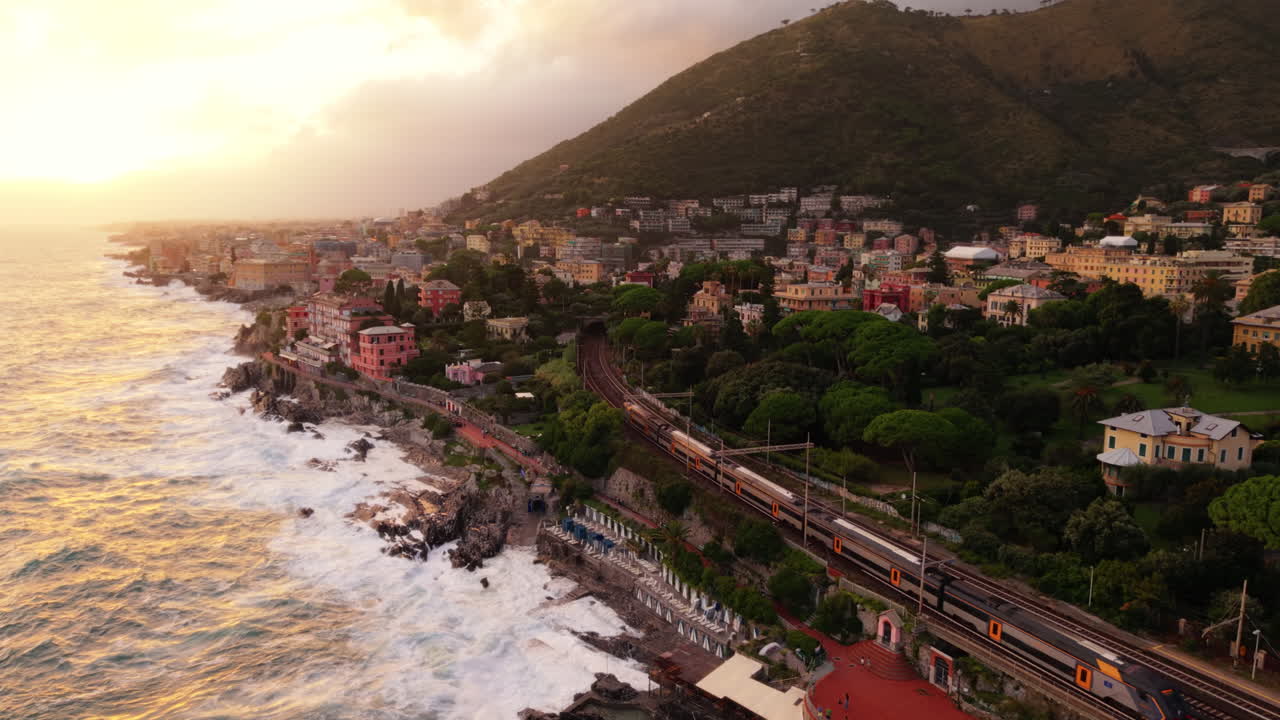 Aerial view of coastal town with train, waves crash in slow motion