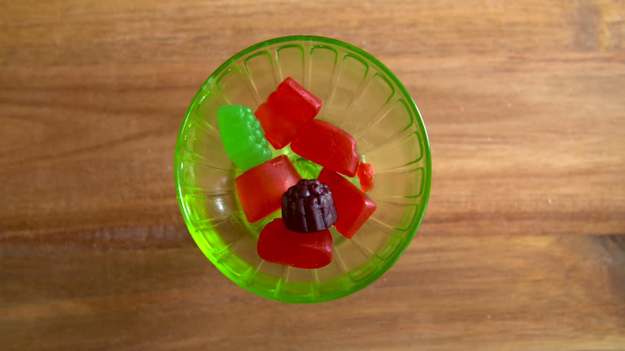 Top down shot of hands taking gummy candies out of a glass dish