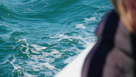 close up of blue ocean wake beside boat with passenger looking over water, 4k australia