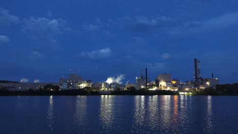 Beleuchtete-Industriefabrik-Mit-Rauch,-Der-Am-Frühen-Morgen-Am-Fluss-In-Michigan-Aufsteigt