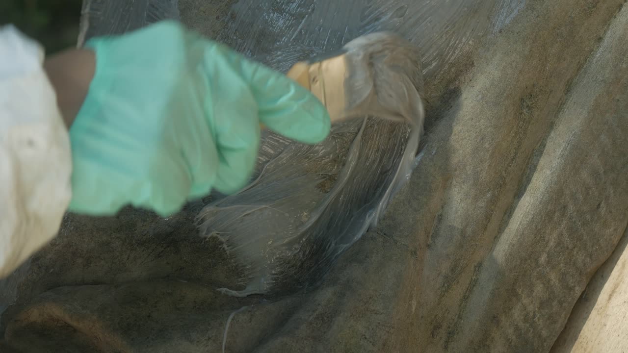 en guante de mano poniendo silicona en las superficies de antiguas esculturas de piedra