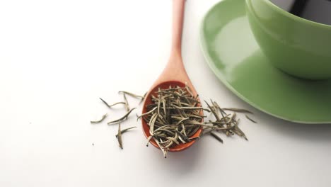 té blanco en cuchara de madera con taza de té verde