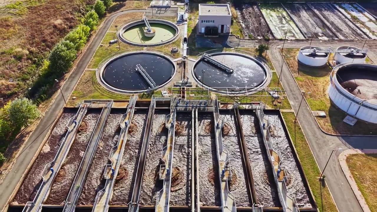 Wastewater treatment facility shows large circular tanks and equipment for processing water located outside a city