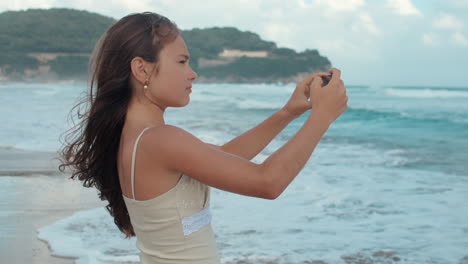 Happy-girl-spending-summer-holiday-at-seaside.-Teenager-filming-on-smartphone.