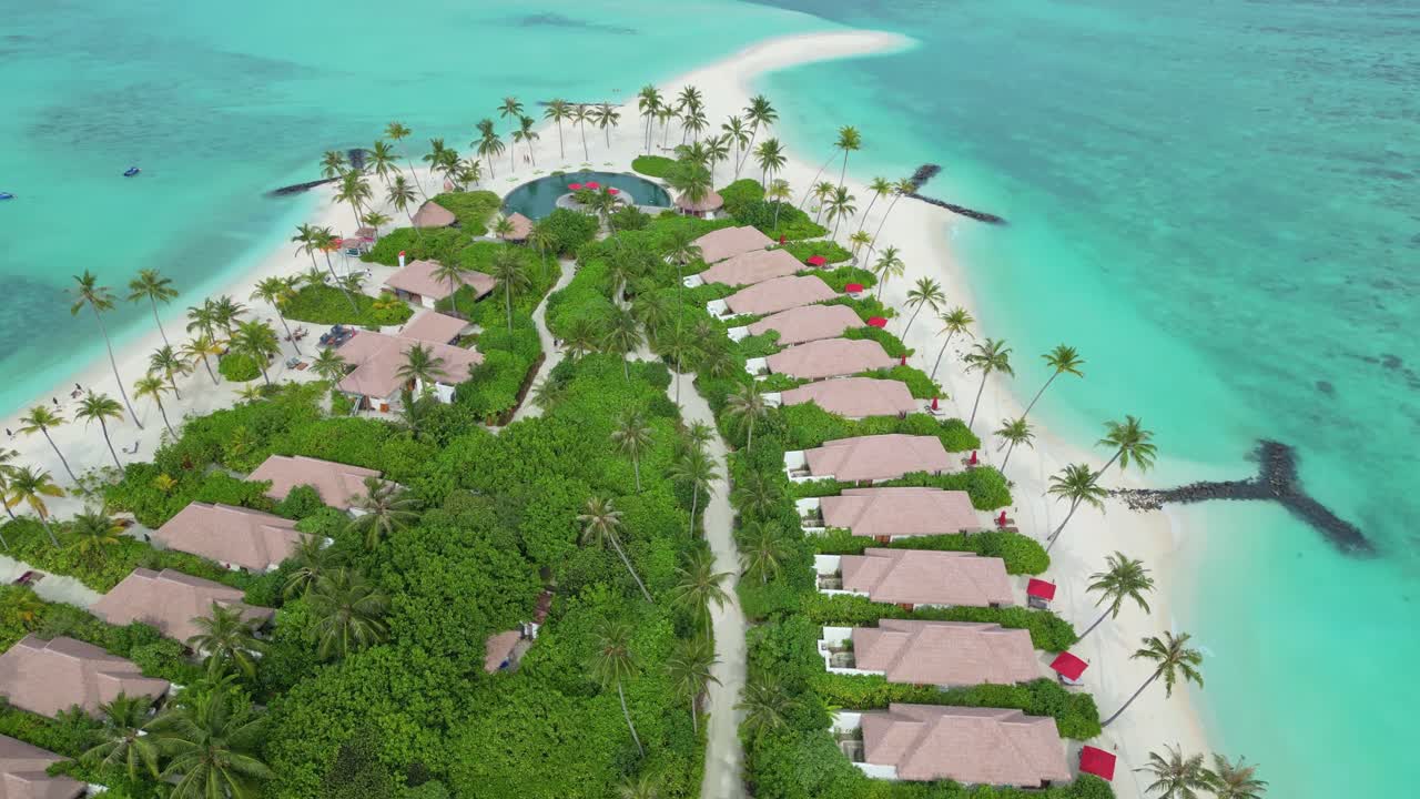 Beach resort with thatched roof villas, palm trees, turquoise waters, white sand beach, Maldives. Aerial tilt down forward