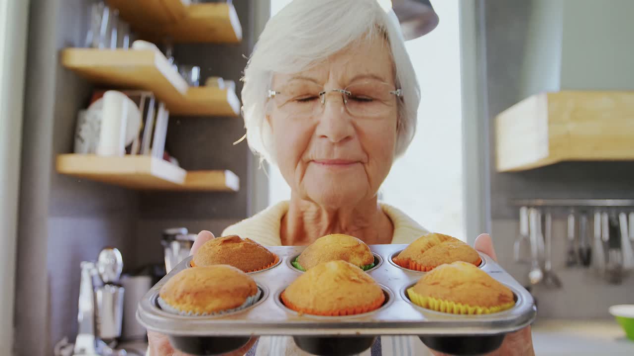 Nonna che tiene una teglia per muffin e annusa i muffin freschi 4K 4k