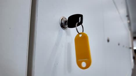 Close-up-view-of-a-key-inserted-in-a-keyhole-with-a-yellow-key-tag-hanging,-against-a-white-background