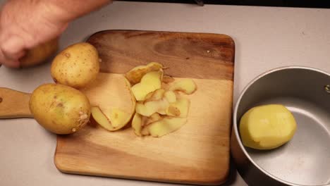 older man’s hands holding a knife and peeling potatoes and putting them in a saucepan.