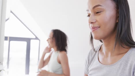 Happy-biracial-lesbian-couple-using-face-cream-and-talking-at-mirrors-in-sunny-bathroom,-slow-motion