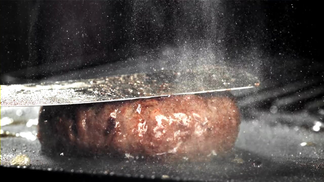 Nærbillede af en burgerbøf, der syder på en varm grill