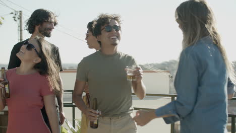 happy friends drinking beer and dancing at rooftop party on a summer day