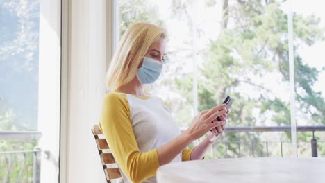 woman wearing face mask using smartphone at home