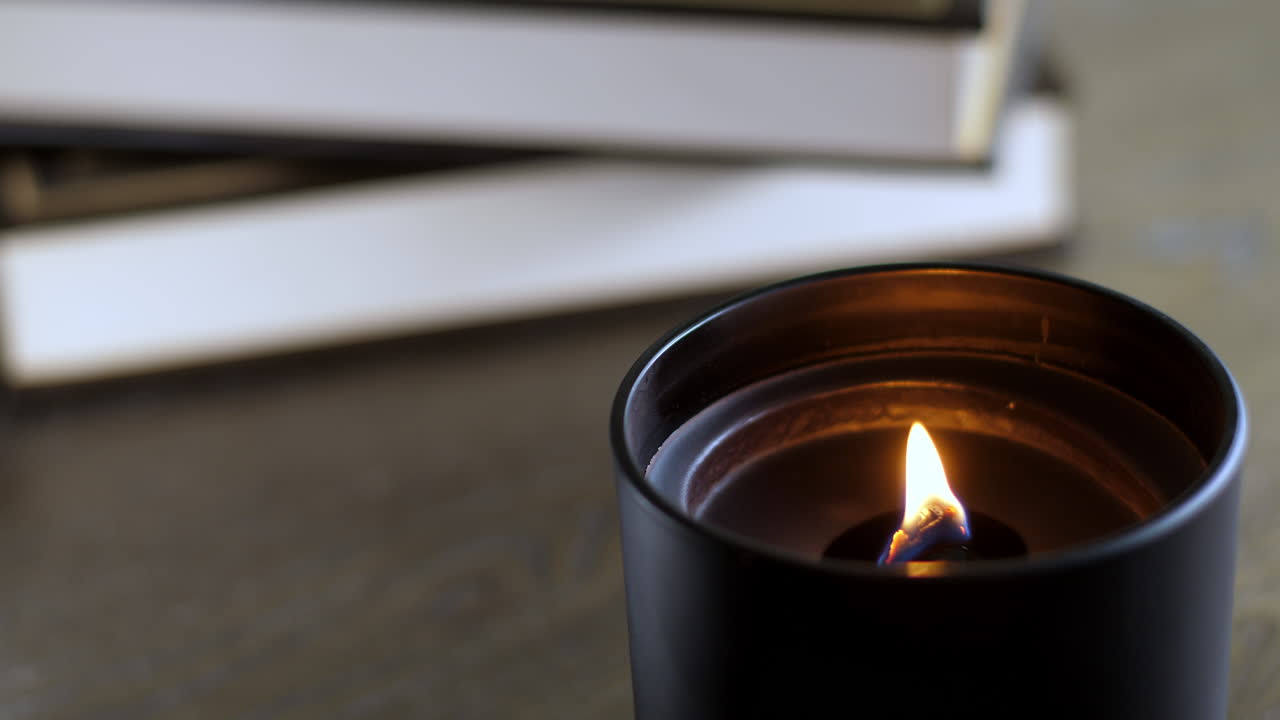 Une bougie noire sur une table basse devant une petite pile de livres