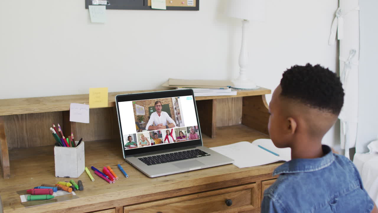 Schoolboy using laptop for online lesson at home, with diverse teacher and class on screen