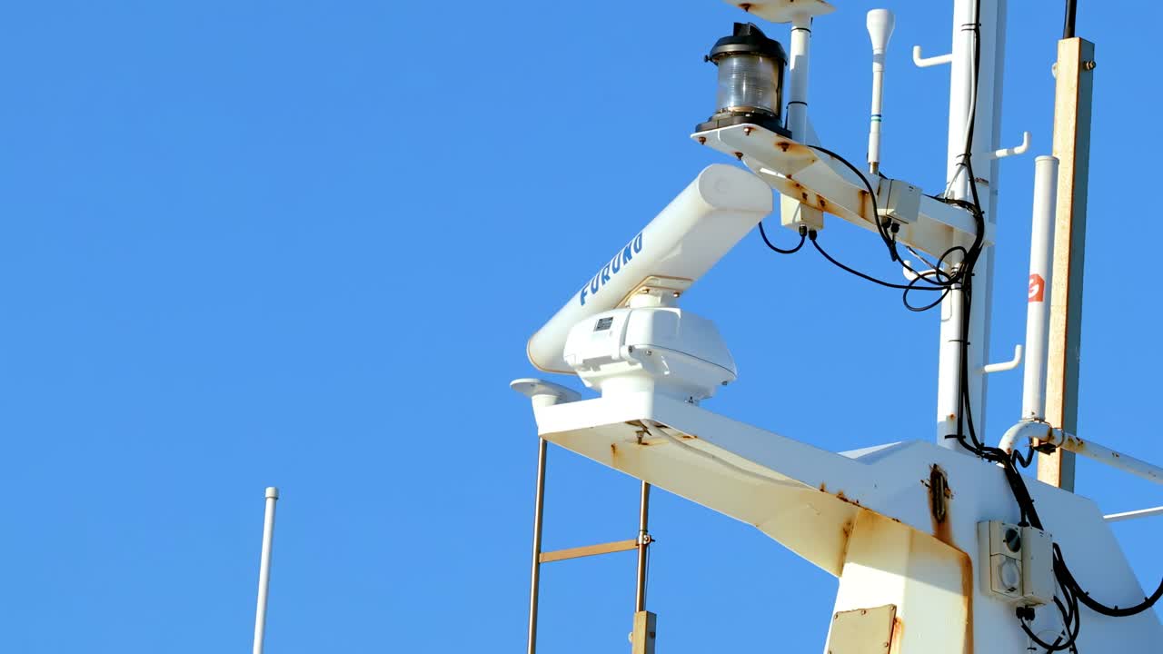 Close-up of a rotating Furuno radar on a ship mast, set against a bright blue sky.